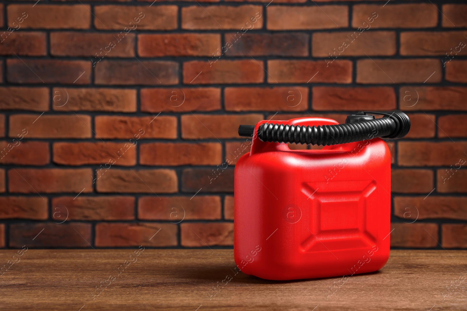 Photo of New red plastic canister on wooden table against brick wall, space for text