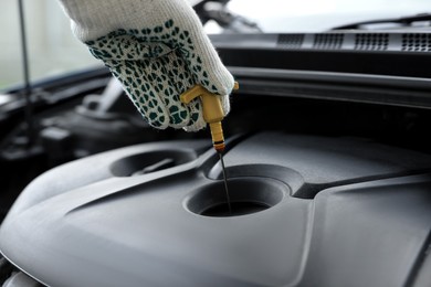Photo of Man checking motor oil level with dipstick in car engine, closeup