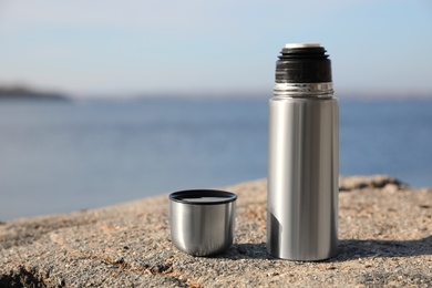 Photo of Aluminium thermos with hot drink on rock stone outdoors. Space for text