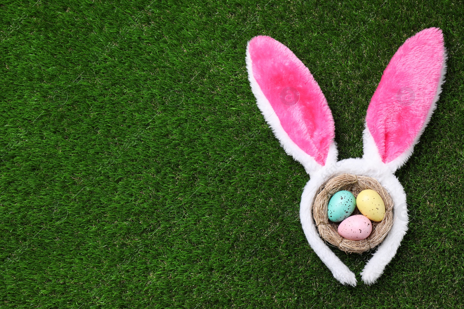 Photo of Headband with bunny ears, painted eggs and space for text on grass, flat lay. Easter holiday