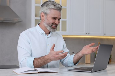 Photo of Man waving hello during video chat via laptop at home