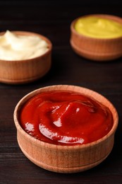 Photo of Ketchup, mustard and mayonnaise in bowls on wooden table, closeup