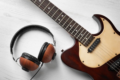Modern electric guitar with headphones on wooden background, top view. Musical instrument