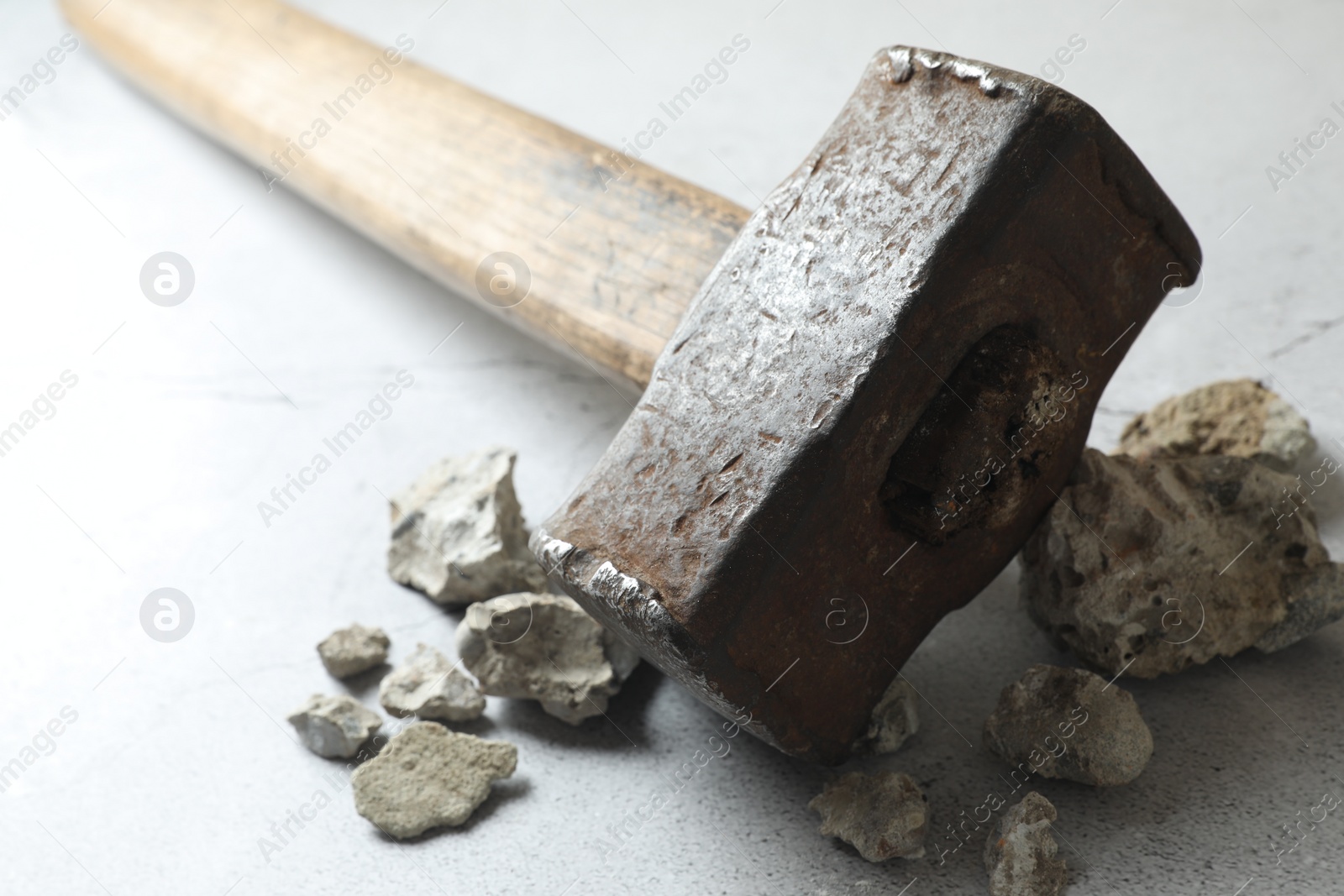 Photo of One sledgehammer and pieces of broken stones on grey textured background, closeup