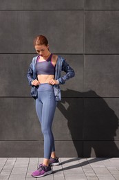 Photo of Beautiful woman in stylish gym clothes near dark grey wall on street