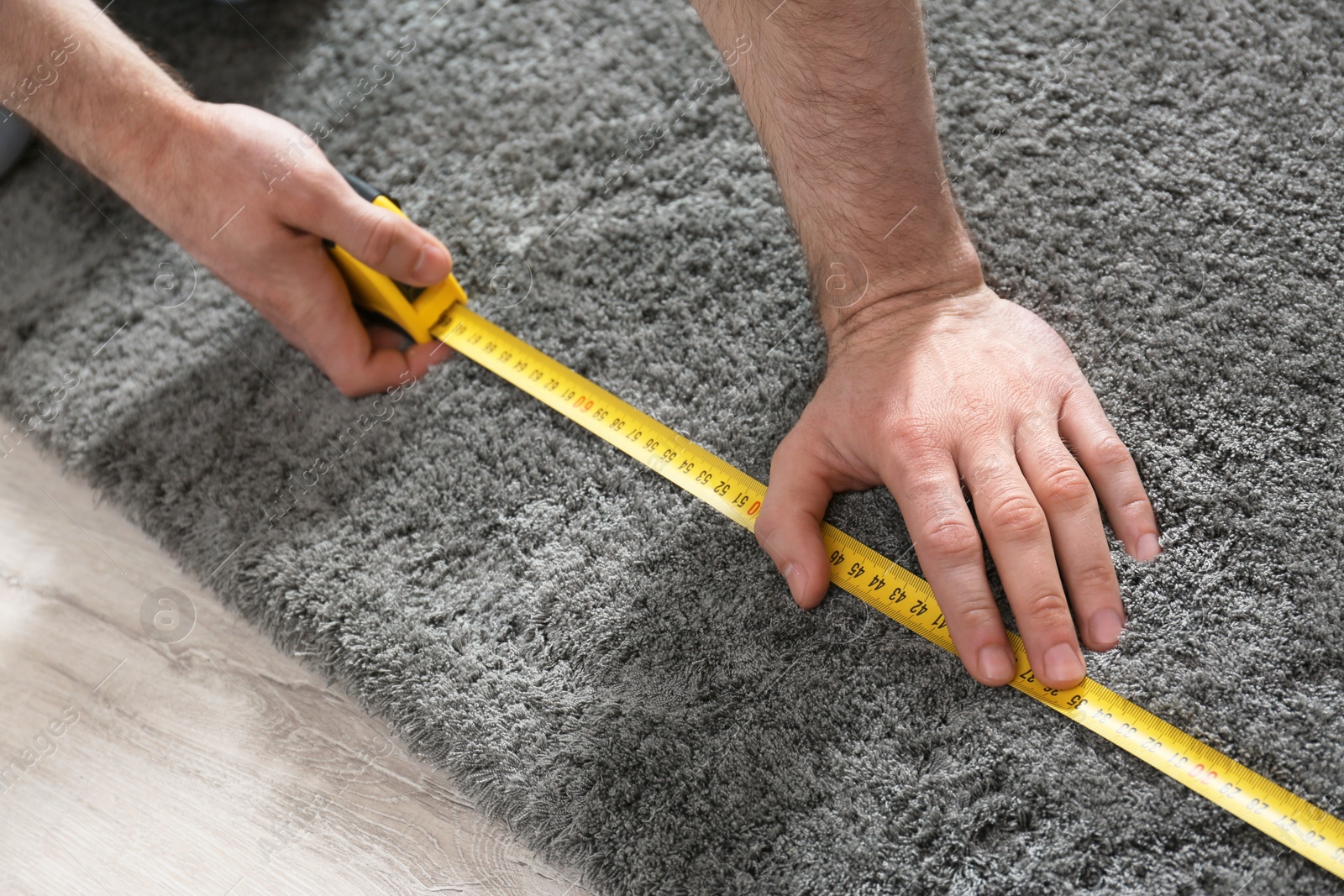 Photo of Man measuring grey fluffy carpet indoors, closeup. Construction tool