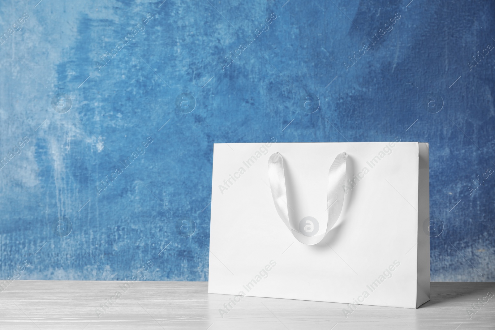 Photo of Paper shopping bag with handles on table against color wall. Mock up for design