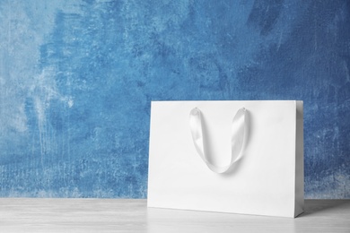 Paper shopping bag with handles on table against color wall. Mock up for design