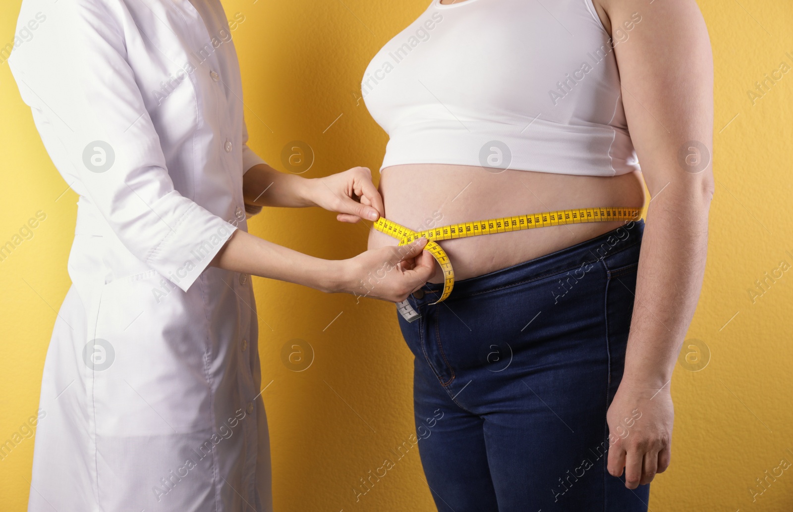 Photo of Doctor measuring waist of overweight woman on color background, closeup