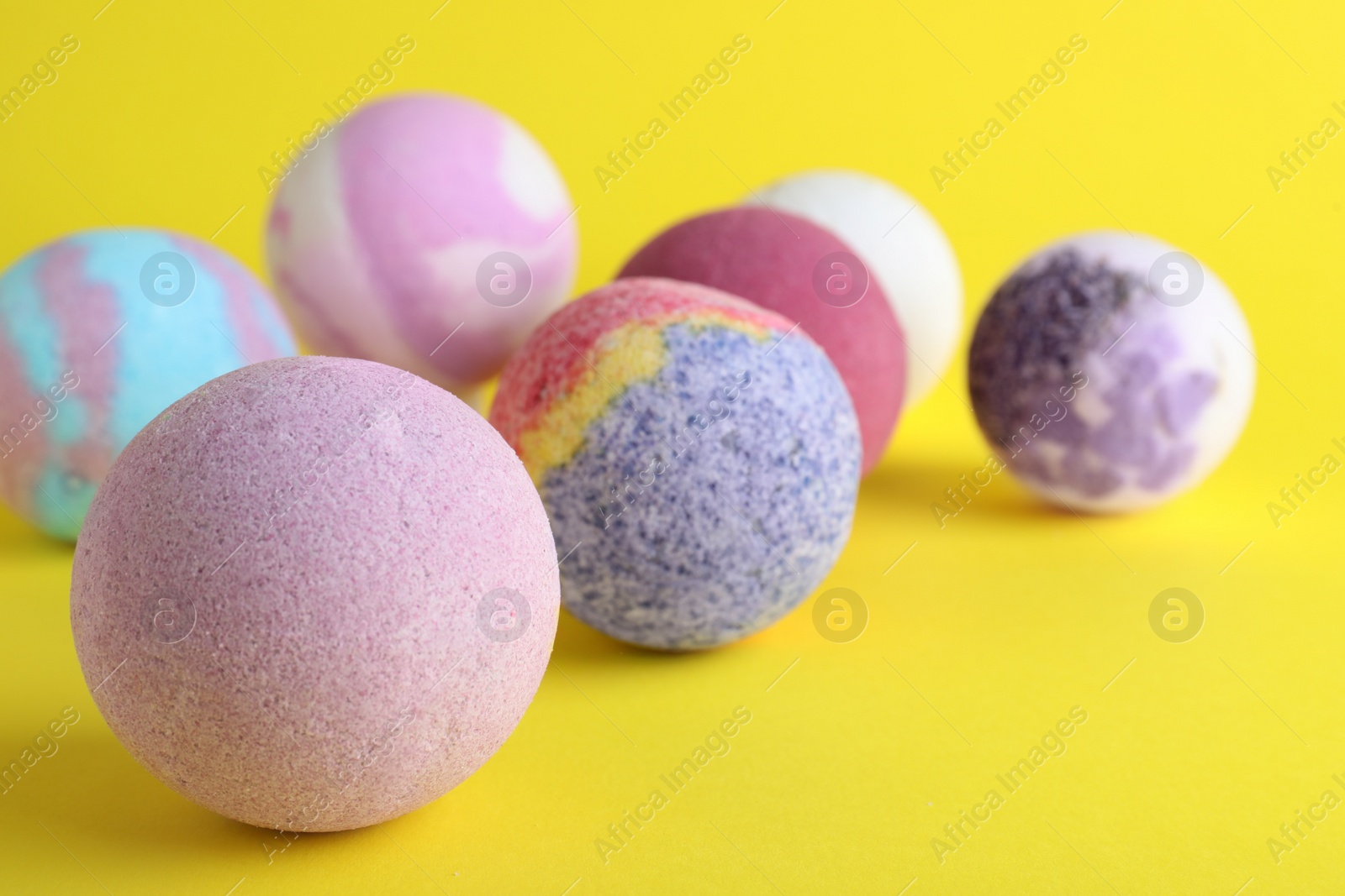 Photo of Colorful bath bombs on yellow background, closeup