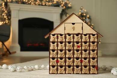 Photo of Wooden house shaped Advent calendar in room decorated for New Year, space for text