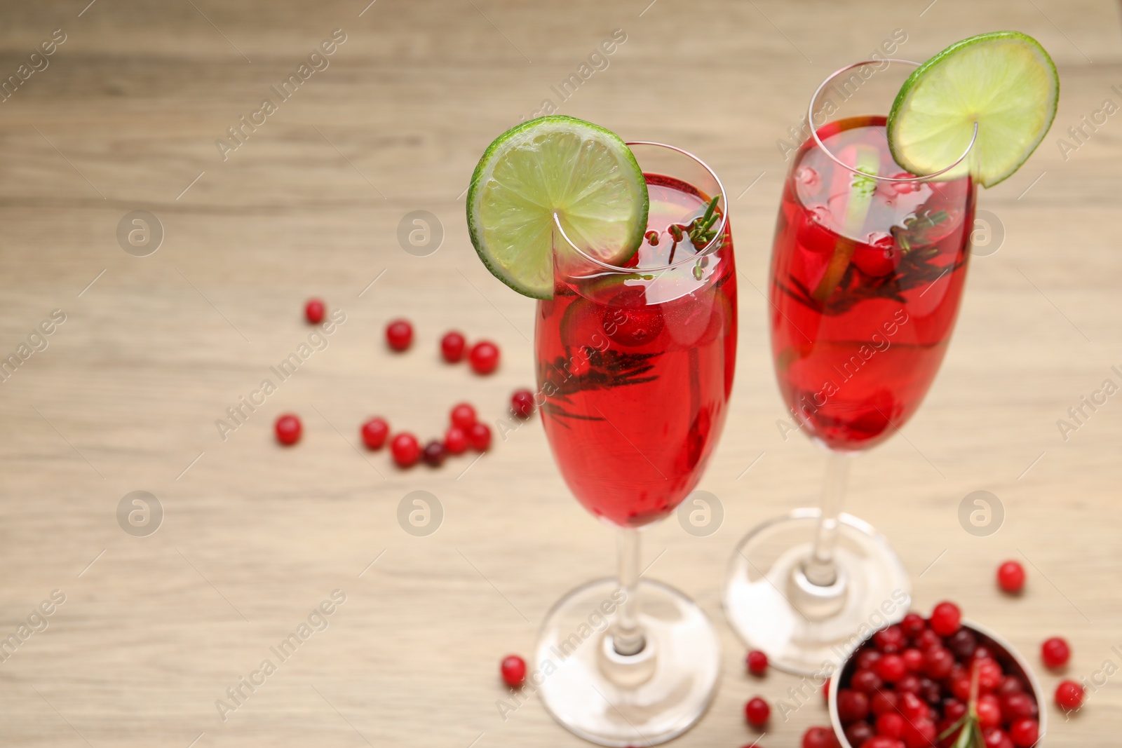 Photo of Tasty cranberry cocktail with rosemary and lime in glasses on wooden table, space for text
