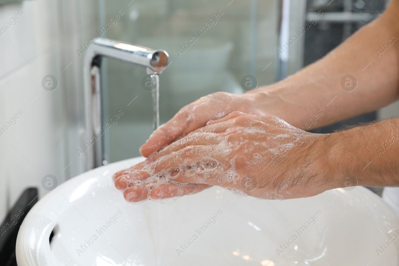 Photo of Man washing hands with soap over sink in bathroom, closeup