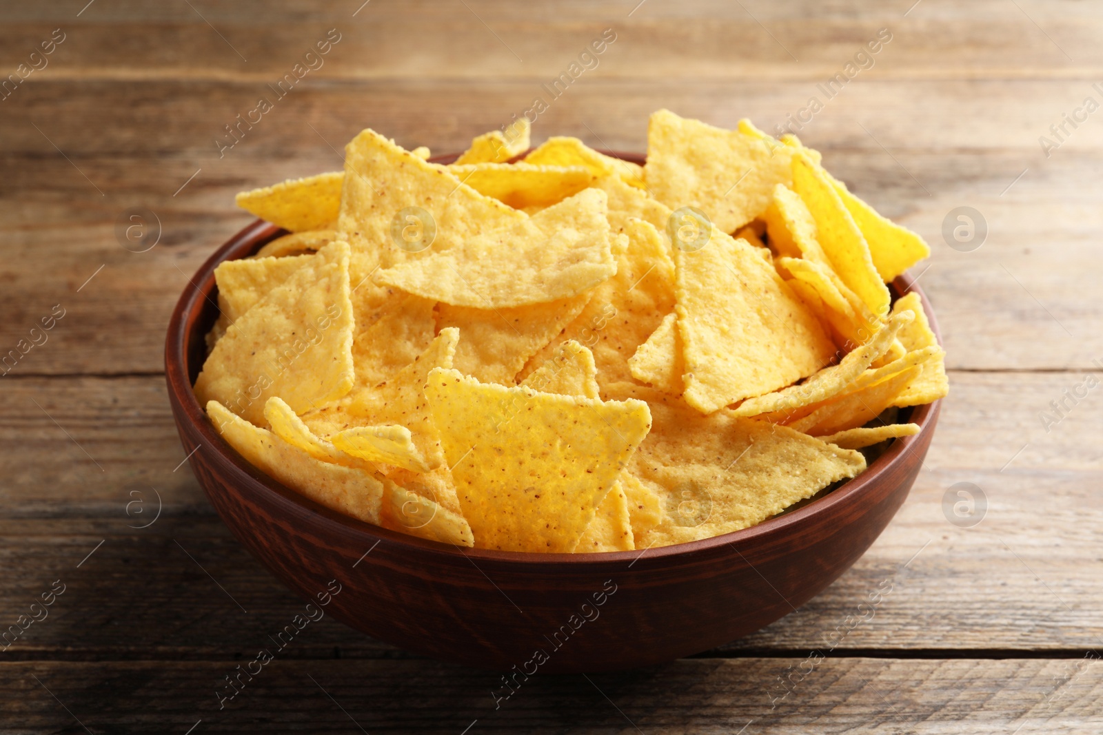 Photo of Bowl with tasty tortilla chips (nachos) on wooden table