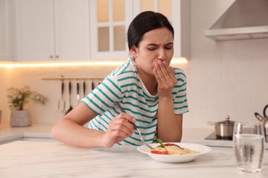 Photo of Young woman feeling nausea while eating at table in kitchen