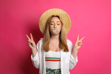 Photo of Fashionable young woman with bright makeup blowing bubblegum on pink background