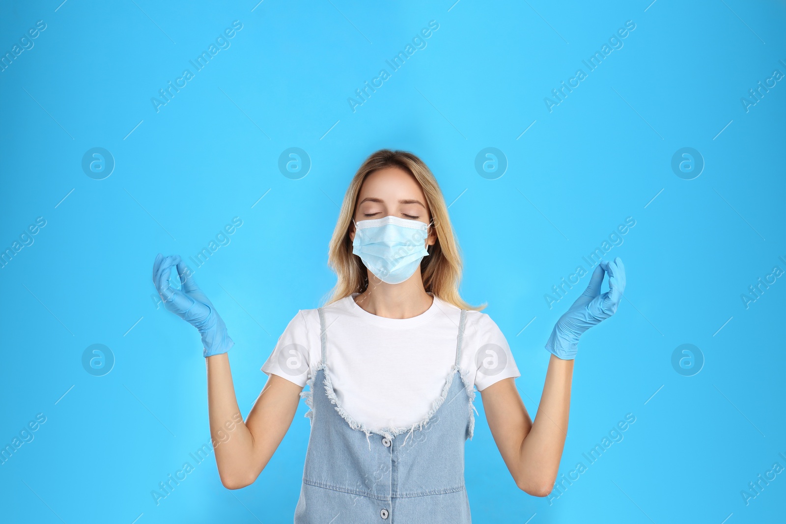 Photo of Woman in protective mask meditating on light blue background. Dealing with stress caused by COVID‑19 pandemic