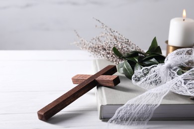 Photo of Burning candle, bouquet with willow branches, book and cross on white wooden table