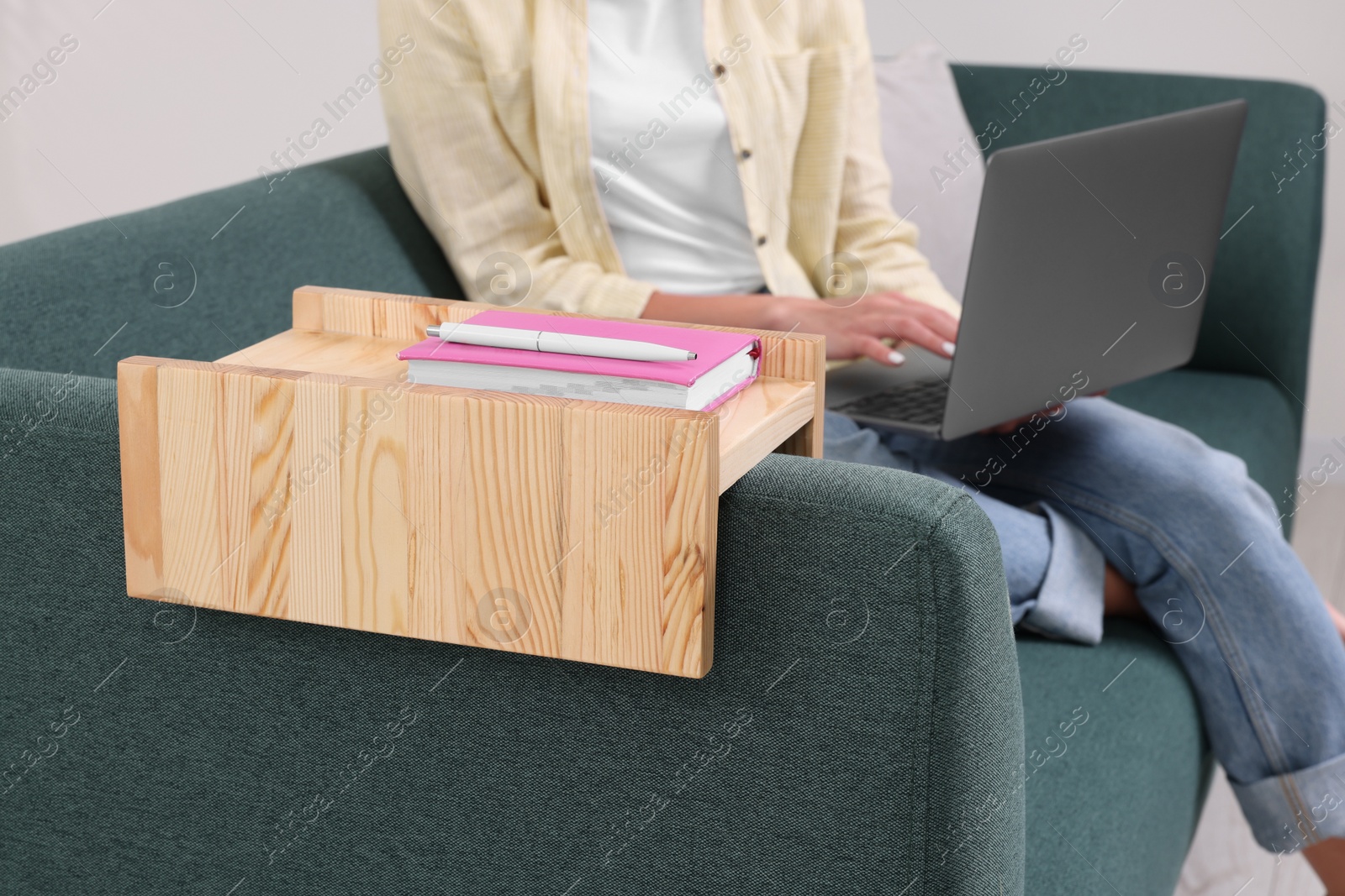 Photo of Notebook and pen on sofa armrest wooden table. Woman using laptop at home, closeup