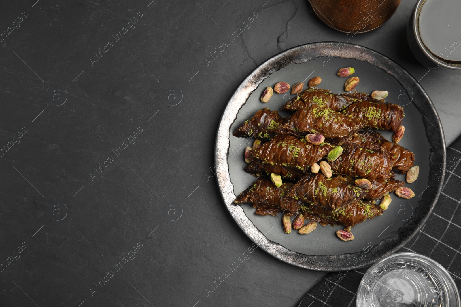 Photo of Delicious baklava with pistachio nuts on black table, flat lay. Space for text