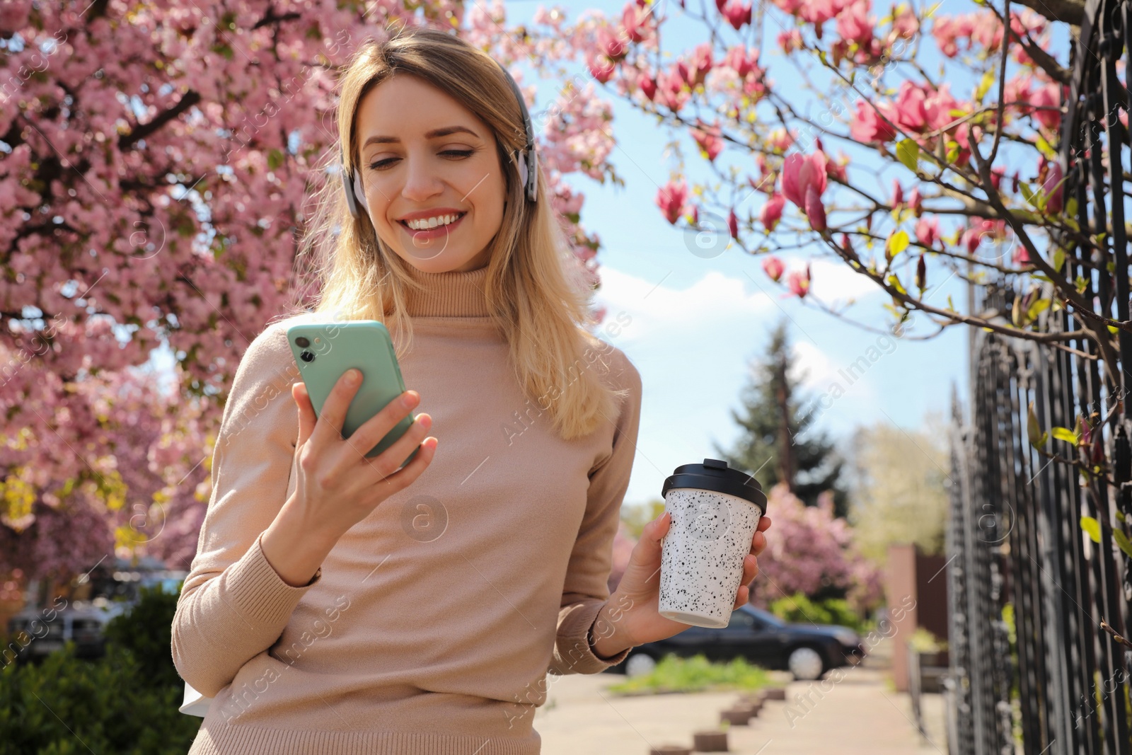 Photo of Happy woman with smartphone and coffee listening to audiobook outdoors on spring day