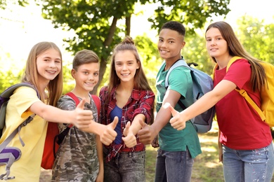 Photo of Group of children showing thumbs up outdoors. Summer camp