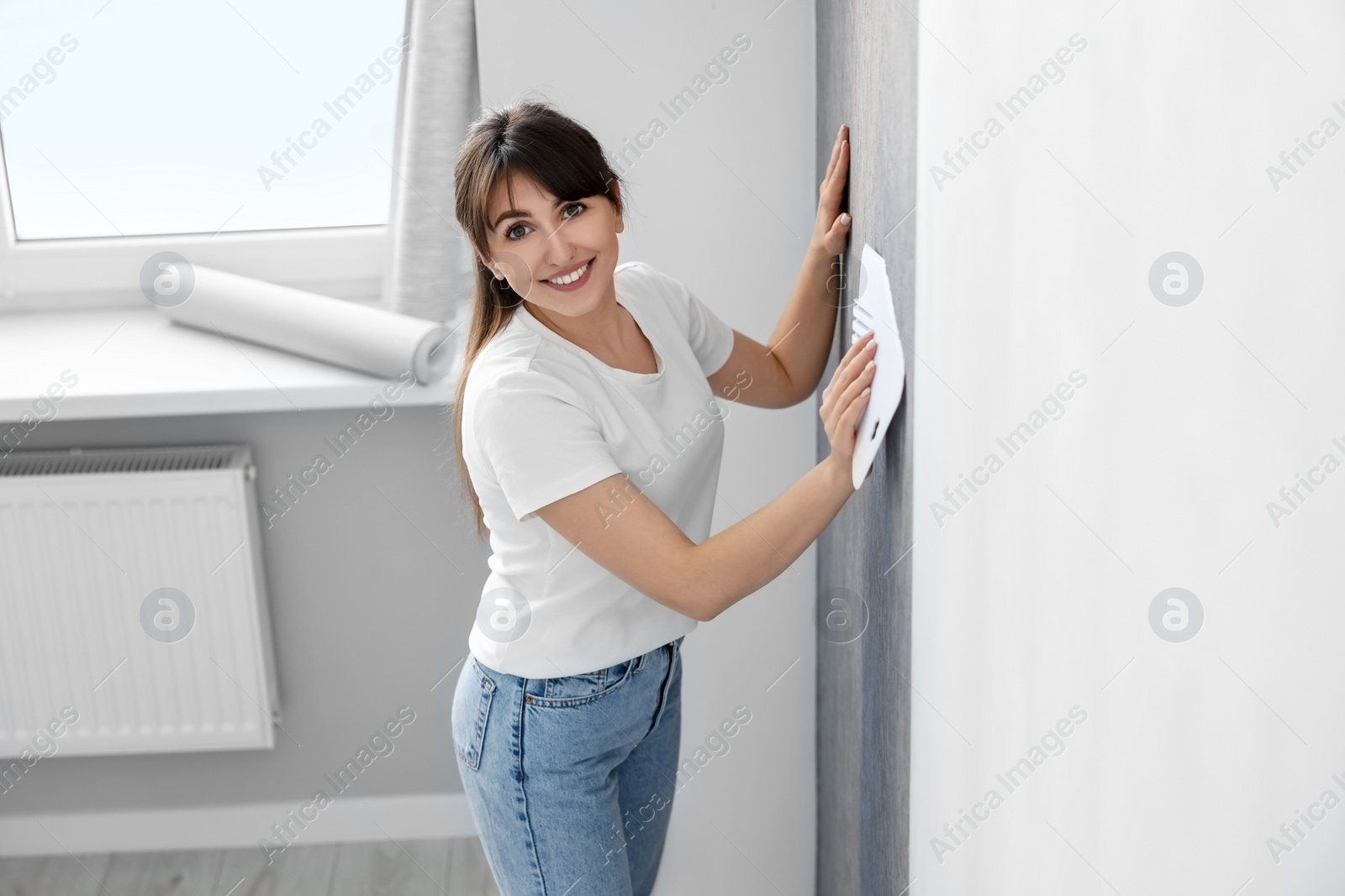 Photo of Woman smoothing stylish gray wallpaper in room