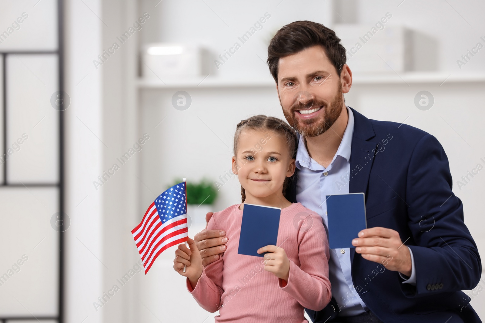 Photo of Immigration. Happy man with his daughter holding passports and American flag indoors, space for text