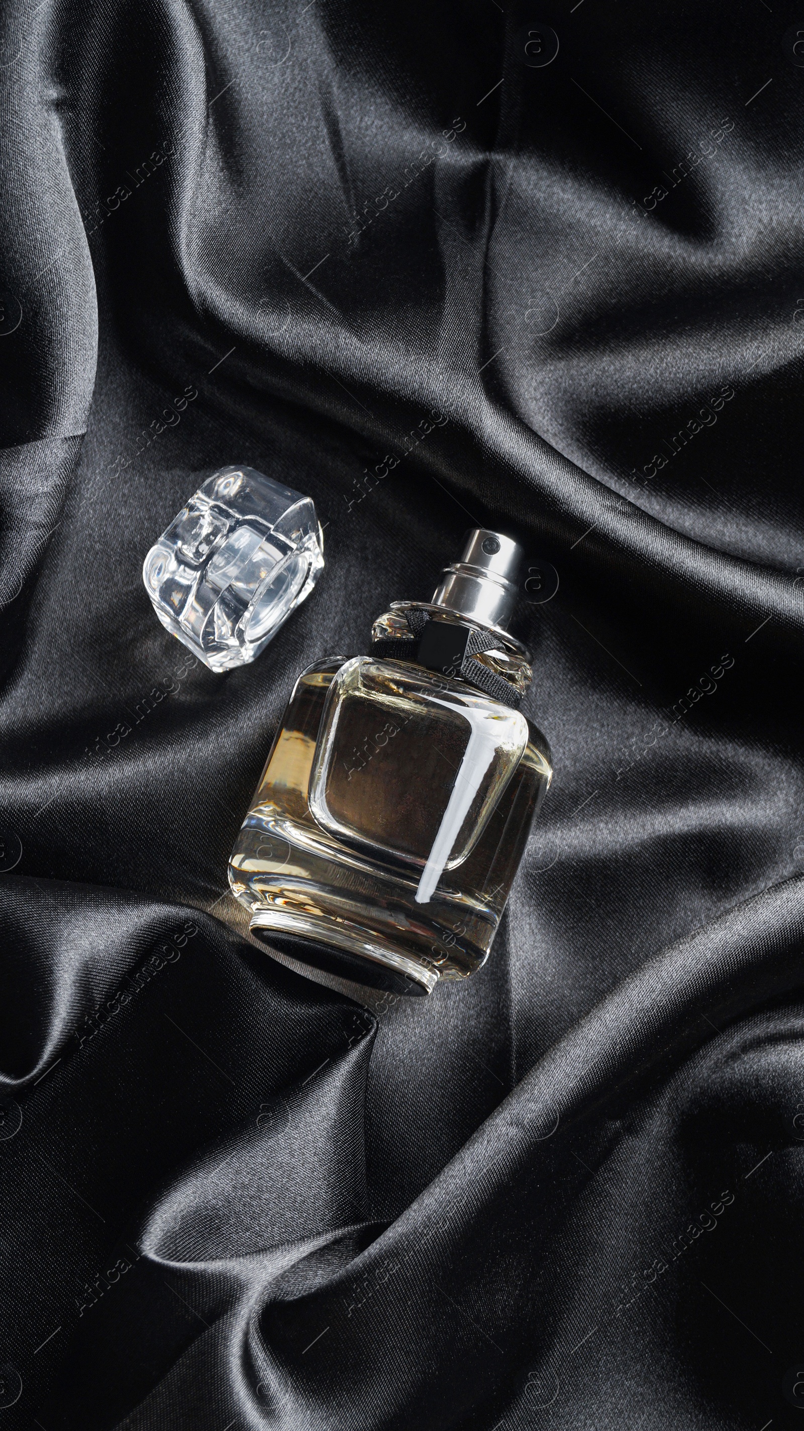 Photo of Luxury bottle of perfume on black silk, top view