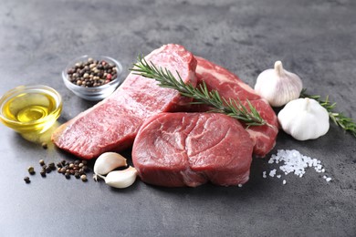 Raw beef steaks, oil and spices on grey table