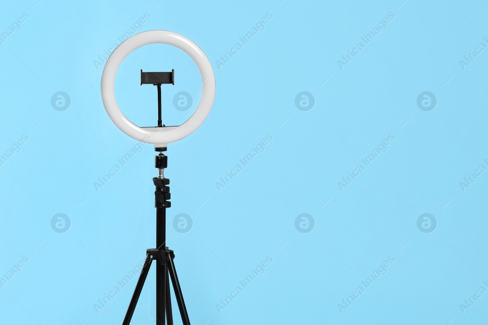 Photo of Modern tripod with ring light on blue background. Space for text