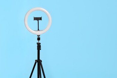 Modern tripod with ring light on blue background. Space for text