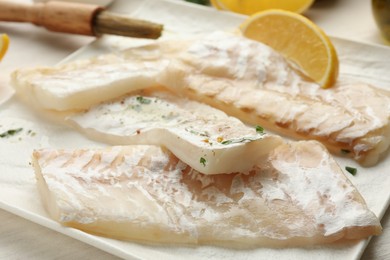 Photo of Fresh raw cod fillets with spices and lemon on table, closeup