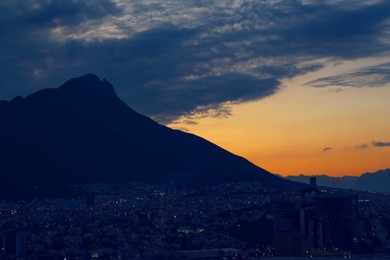 Photo of Picturesque view of sunset with dark clouds above big mountains and evening city