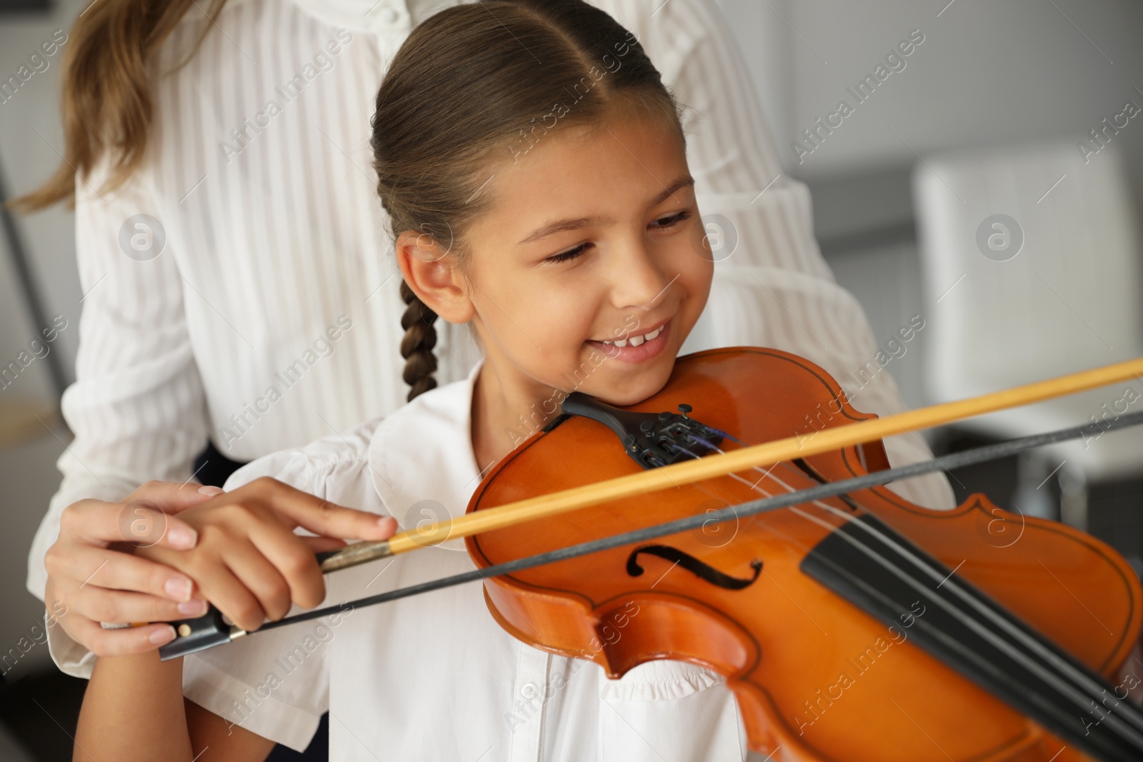 Photo of Young woman teaching little girl to play violin indoors