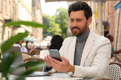 Photo of Handsome man using smartphone at table in outdoor cafe