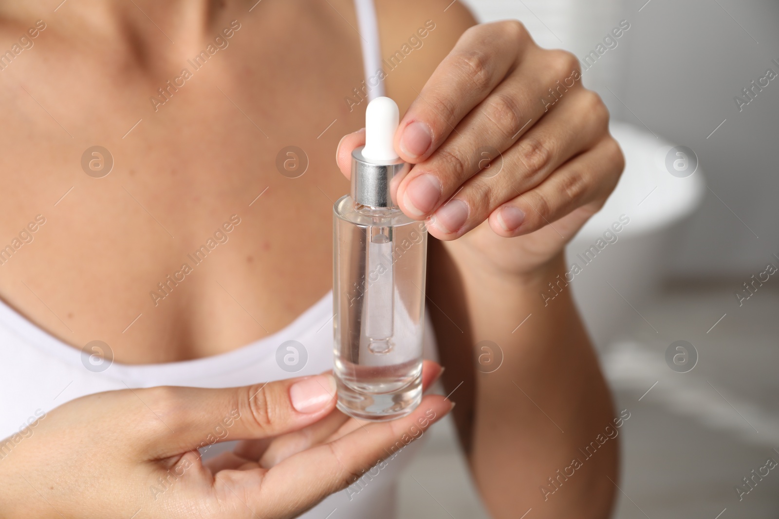 Photo of Woman with bottle of cosmetic serum on blurred background, closeup