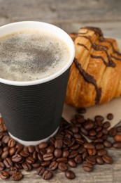 Photo of Coffee to go. Paper cup with tasty drink, beans and croissant on wooden table, closeup
