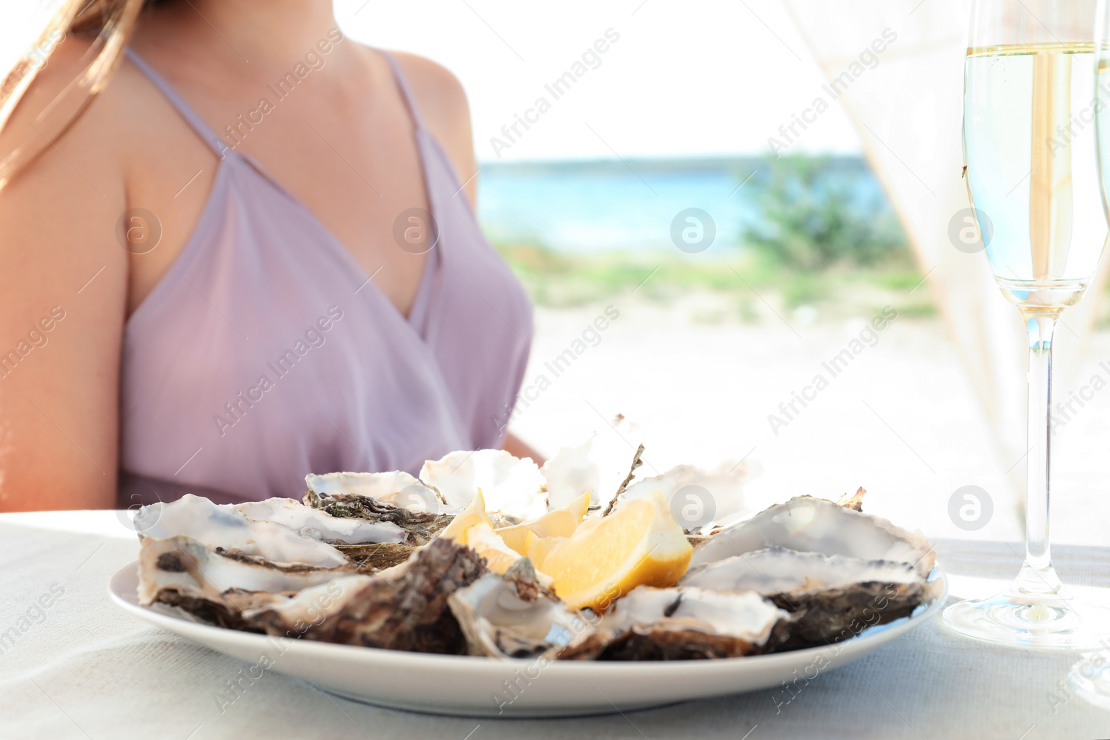 Photo of Woman with fresh oysters and cut juicy lemon at table