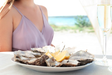 Photo of Woman with fresh oysters and cut juicy lemon at table