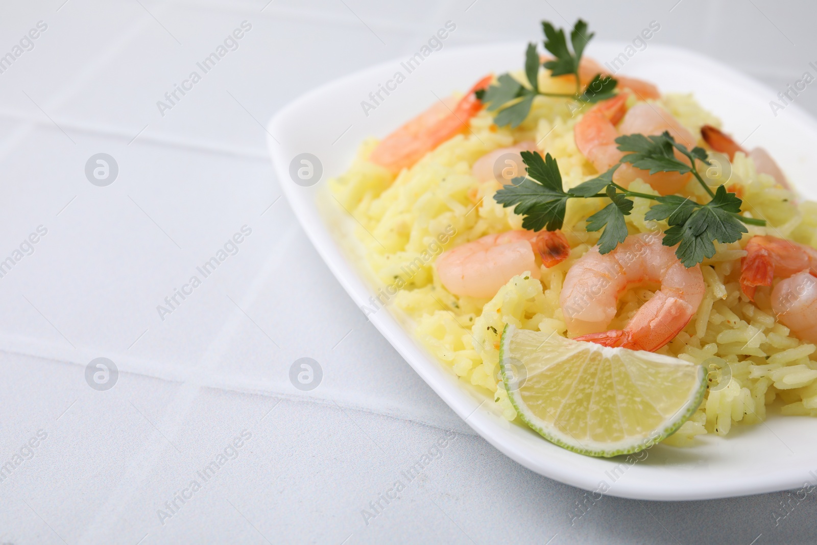 Photo of Delicious risotto with shrimps, lime and parsley on white tiled table, closeup. Space for text