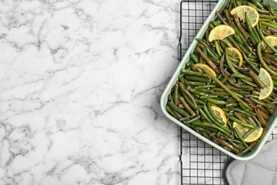 Dish with tasty green beans and lemons on marble table, top view