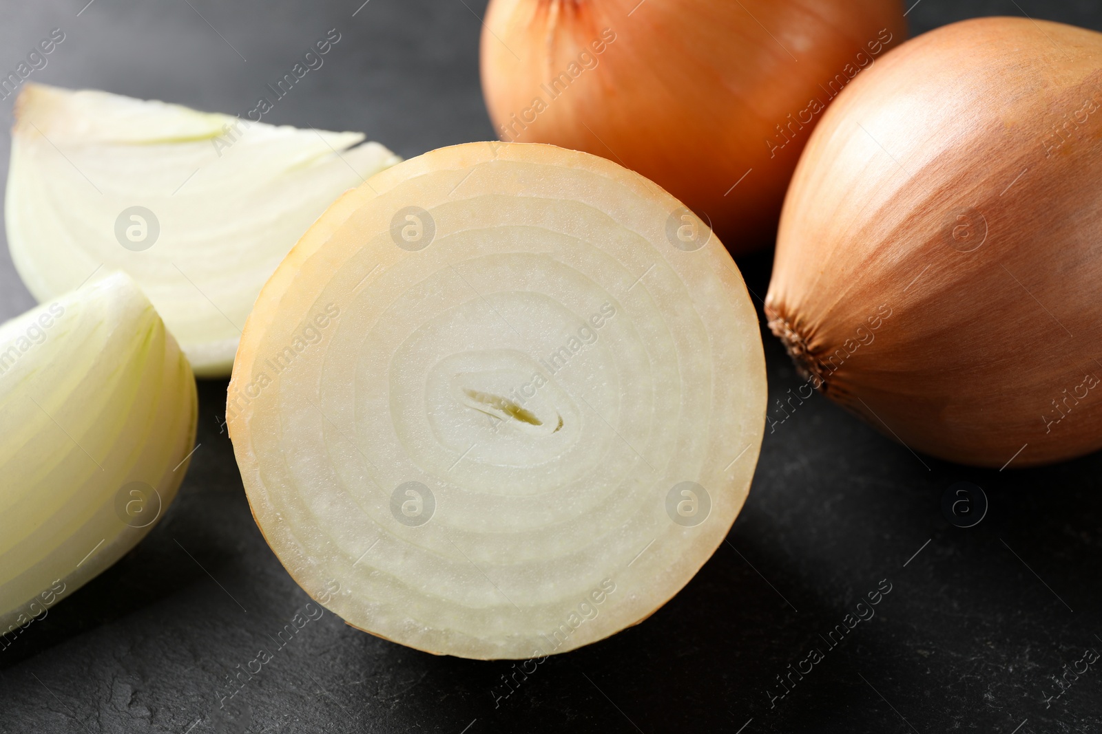 Photo of Whole and cut onions on black textured table, closeup