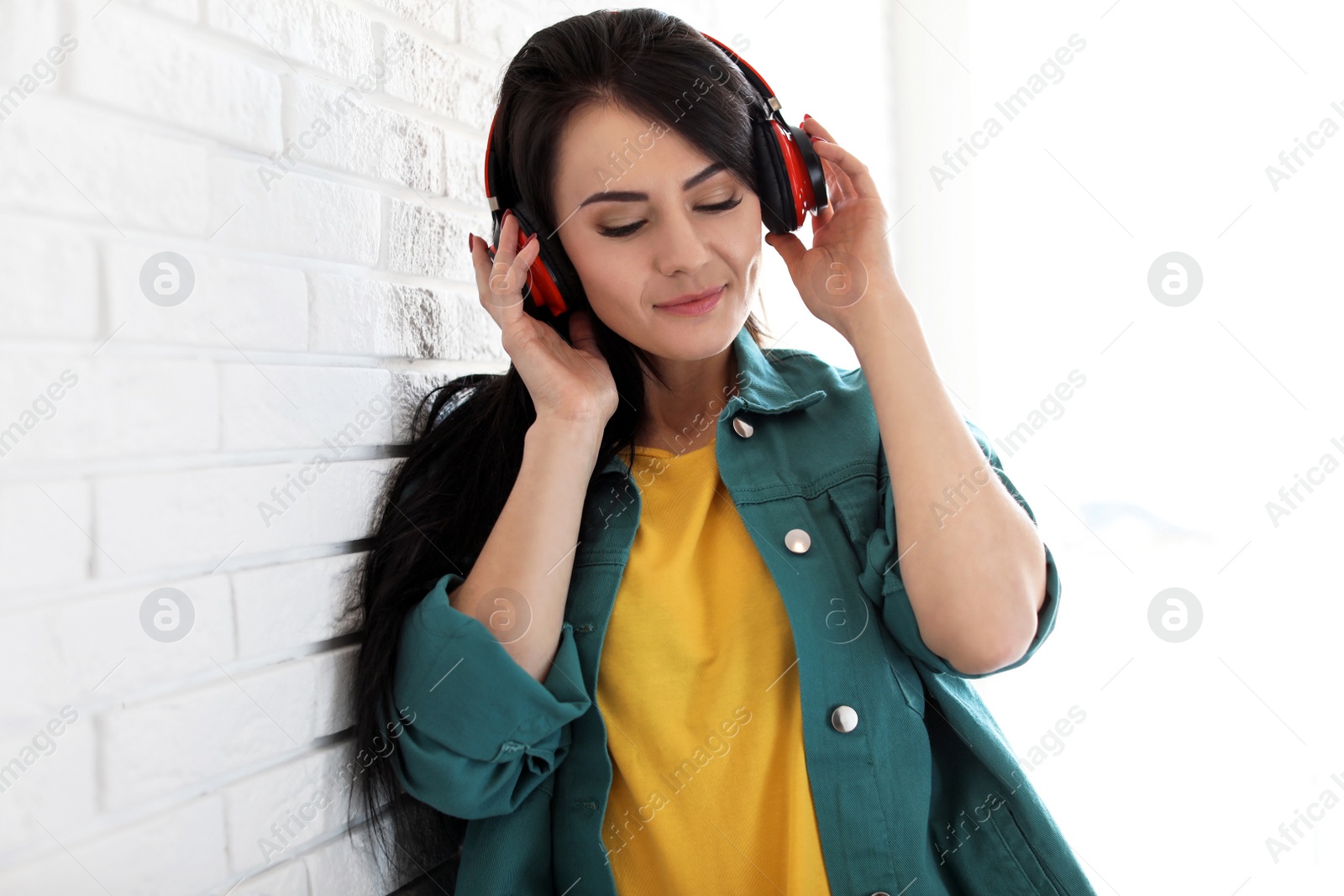 Photo of Portrait of beautiful woman listening to music with headphones near brick wall