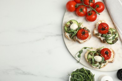 Photo of Tasty bruschettas with capers, vegetables and mozzarella served on white marble table, flat lay. Space for text