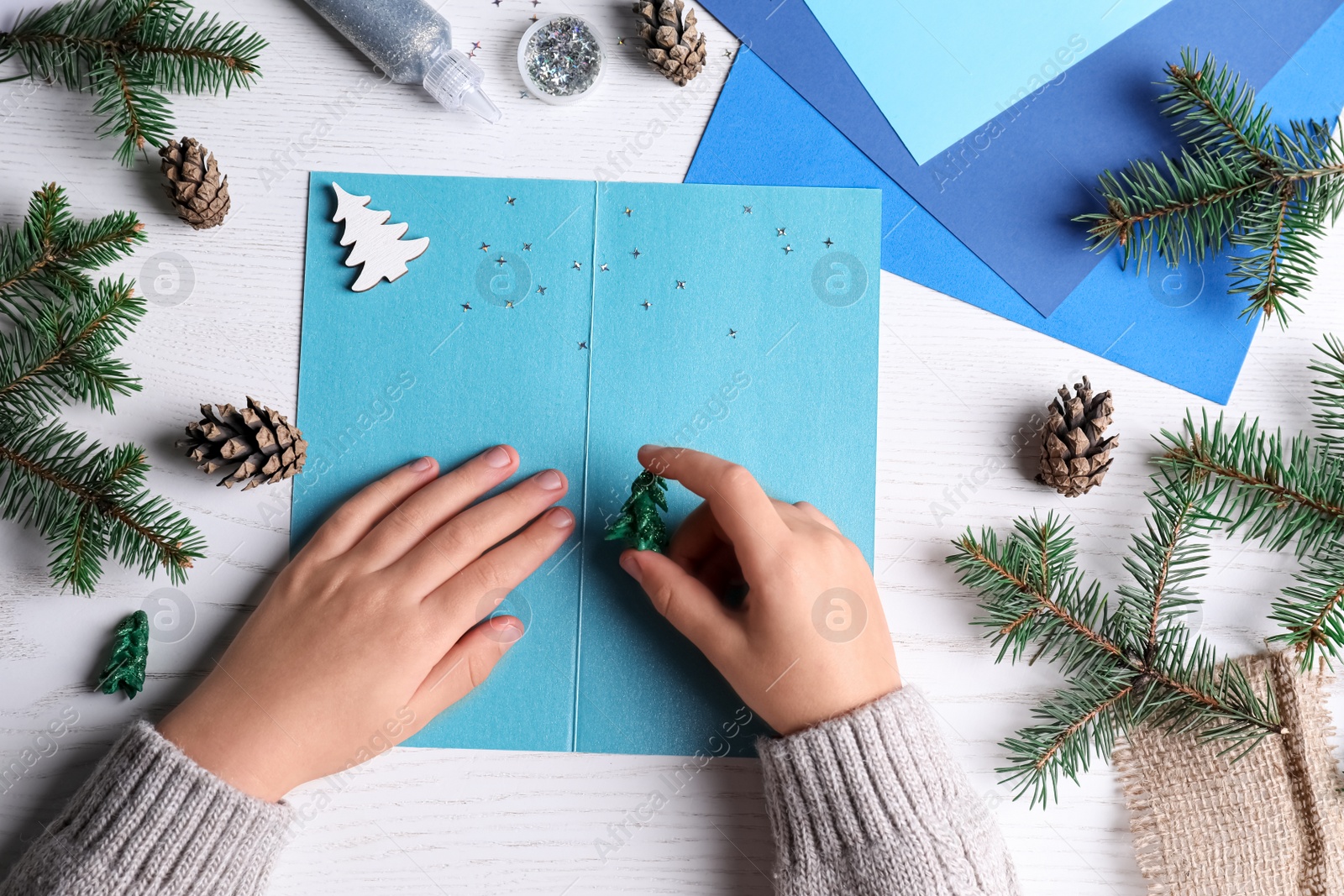 Photo of Little child making Christmas card at white wooden table, top view