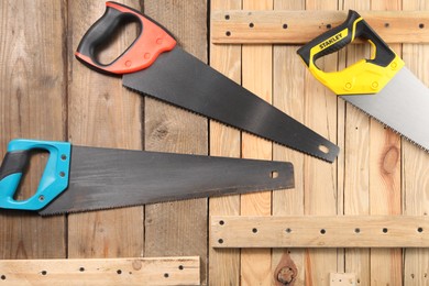 Photo of Saws with colorful handles on wooden surface, flat lay
