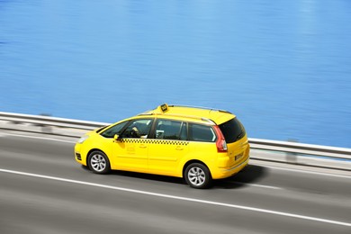 Image of Yellow taxi cab driving at high speed on asphalt road near river outdoors, motion blur effect