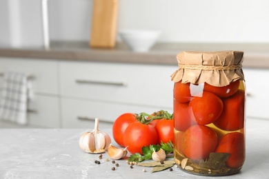 Jar with pickled tomatoes and vegetables on grey table in kitchen. Space for text