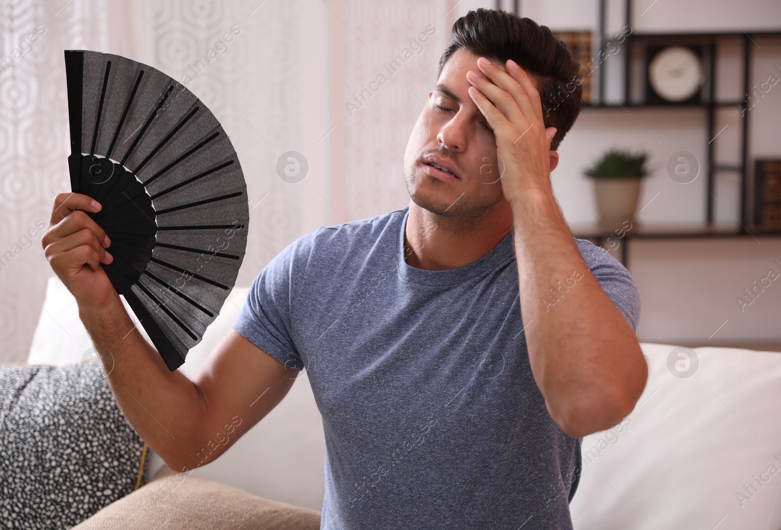 Photo of Man with hand fan sitting on sofa. Summer season